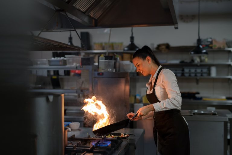 Professional chef preparing meal, flambing indoors in restaurant kitchen